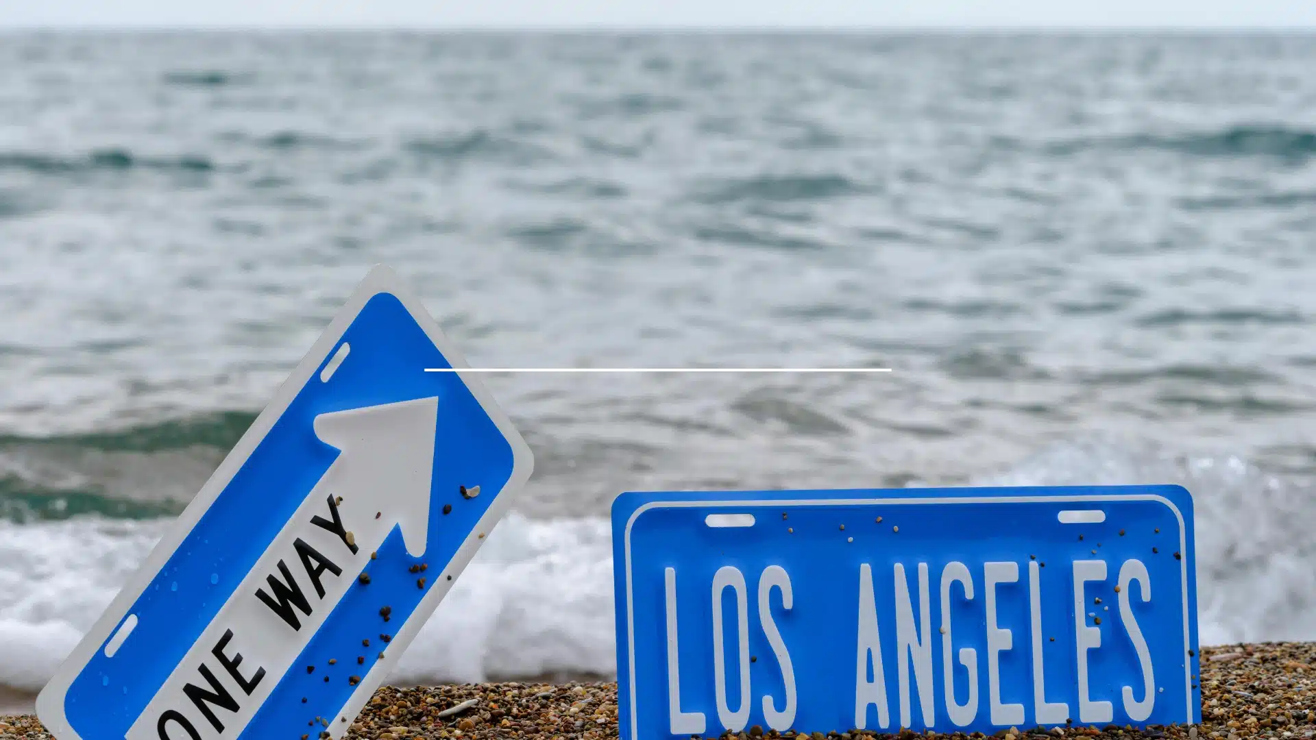 Directional board sign in Los Angeles near a waterfront area with water, sky, and coastal surroundings.