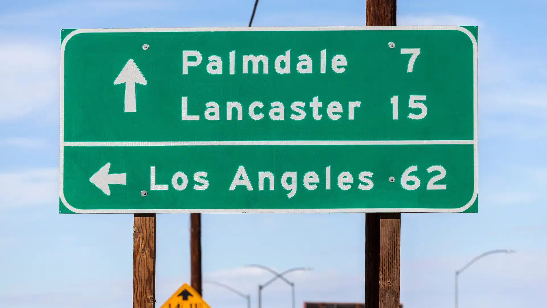Road sign in Palmdale, California showing city direction with desert landscape and open roadway.