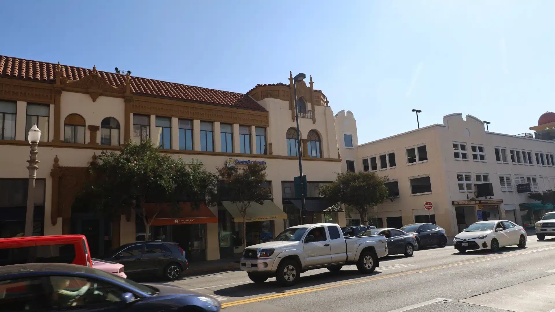 Street view of downtown Pasadena with classic storefronts, parked cars, and sunny weather